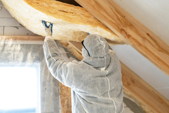 Technician installing fresh insulation along a sloped attic ceiling